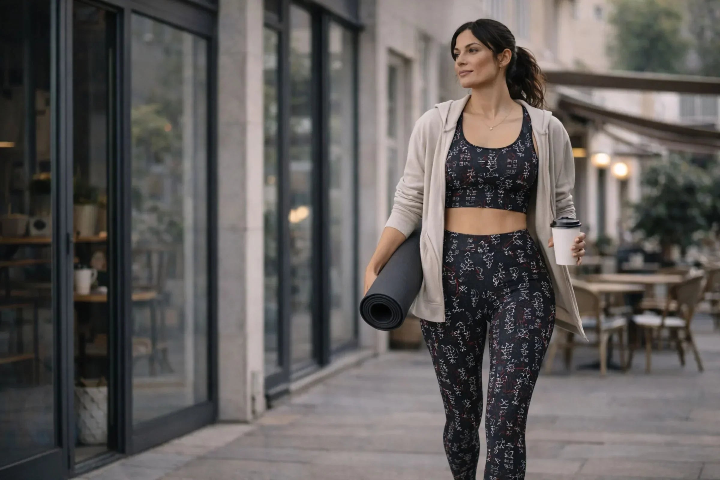 Woman wearing dark-toned studio to street outfit with subtle sacred geometry details walking from yoga studio to city café in refined athleisure look