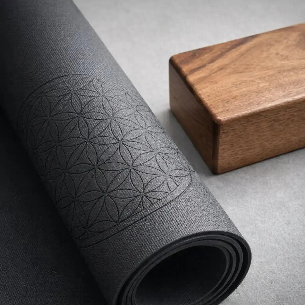 Professional yoga gear with charcoal rubber mat featuring Flower of Life alignment pattern and mango wood yoga block in studio lighting